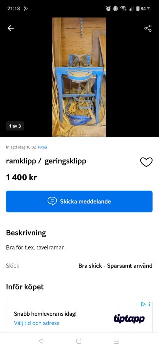Blå ramklippmaskin för geringssnitt, lämplig för tavelramar, placerad i en träverkstad med träbitar och sågspån runtom.