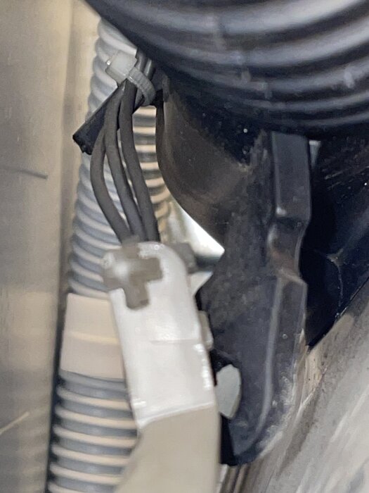 Närbild av kabelbrott under tvättmedelsfacket med sammanbundna kablar och plastclip.