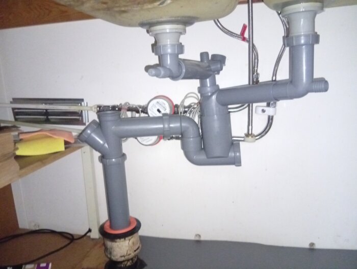 Undersidan av en diskho med rör, kopplingar och eventuell ljudisolerande beläggning syns, möjligtvis orsak till luktproblem.