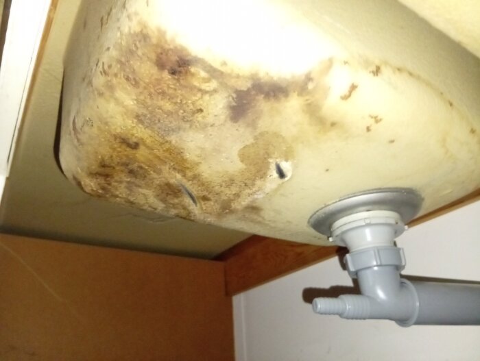 Undersidan av en diskho från 80-talet med märkbart belägg, rör och eventuell vattenskada; utreds för att hitta källan till en frän lukt.