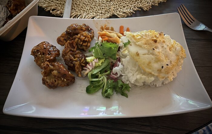 Japansk varmrätt med friterade kycklingbitar, ris, stekt ägg, sallad och picklade grönsaker på en vit tallrik.