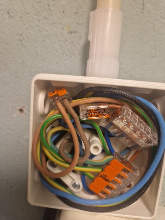 Kopplingsbox med flera färgade ledningar, kopplingsmuffar och dragavlastning monterad på vägg.