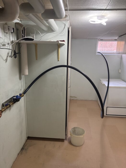 Tillfällig vattenlösning i källare med slang ansluten till vattenrör och hink under för att hantera läcka innan reparation av grävbolag.