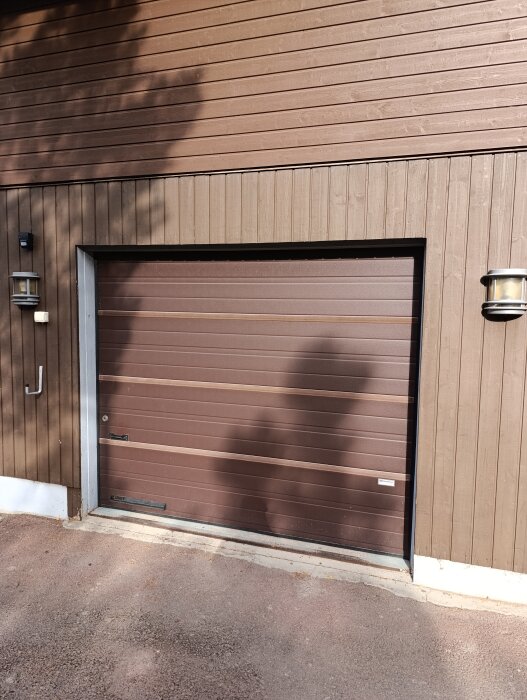 Brun garageport innan breddning, med träpanelade väggar och belysning.