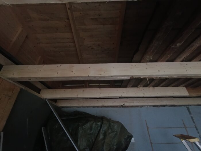 Garagetak med ny träpanel, synliga bjälkar och en presenning i hörnet. Renovationsprocess för att åtgärda fuktskada och uppdatera gipstaket.