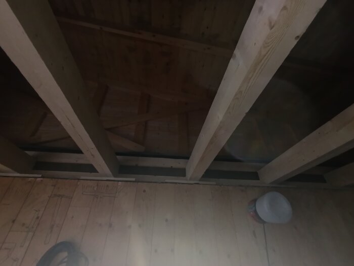 Träbjälkar och tak i ett garage under renovering, med en burk i ena hörnet.