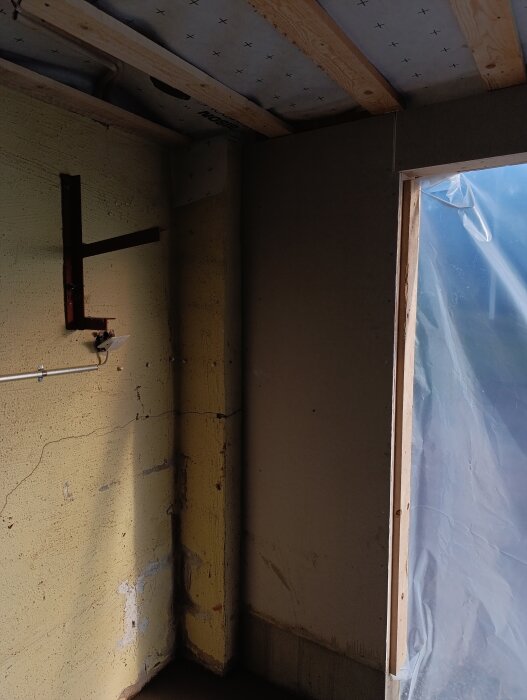 Garagets inre hörn med synlig fuktskada på väggen, träbalkar i taket och en plastskyddad öppning.