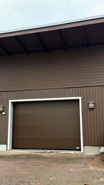 Utsidan av ett brunt garage med vita dörrkanter och två runda vägglampor.