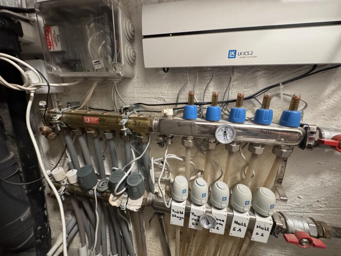 Golvvärmesystem med rör och ställdon under ett LK ICS.2 styrsystem, med manometer och anslutningar för olika rum i ett hus.