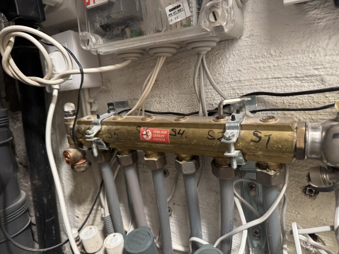 Ventilationssystem med flera rör och en fördelare märkt med "Vorlauf Depart Andata", kopplingar synliga i en teknisk installation.