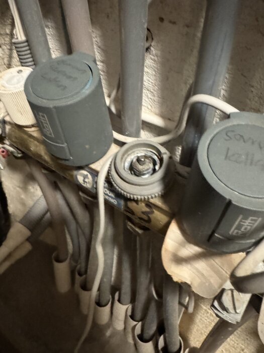 Närbild på ett trasigt ställdon för golvvärme, med sprucken plastring, omgiven av rör och kablar i ett äldre Roth-system.