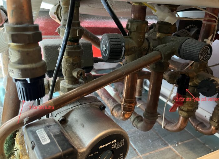 Närbild av värmesystemets rör och ventiler med markeringar för var man luftar och fyller på vatten, enligt instruktioner i Nibe VVM300.