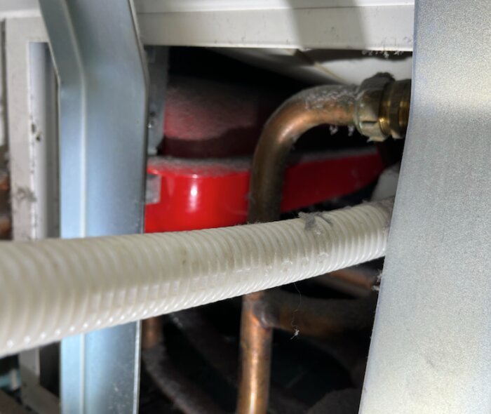 Närbild av rör och komponenter i en Nibe VVM300 värmepump, med fokus på vita och kopparfärgade rör samt en röd del i bakgrunden.