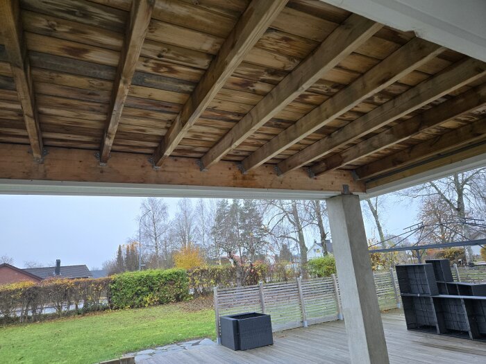 Träbjälklag med limträbalk och balkskor, synliga utomhus på en altan med grönska och höstfärger i bakgrunden.