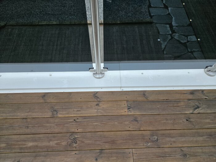Trädäck med metallräcke och synlig skarv mellan trägolv och vit plåt. Möjliga tecken på tidigare fuktproblem under plåten.