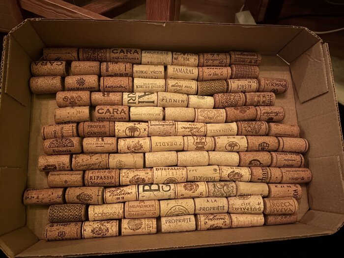 Låda med sorterade vinkorkar, etiketter synliga, i olika nyanser av brunt. Korkarna ligger prydligt arrangerade i mönster.