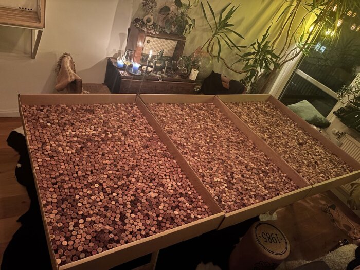 Lådor fyllda med korkar i olika färgnyanser står på ett bord i ett vardagsrum med växter och ljus i bakgrunden.