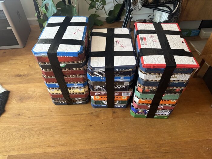 Staplar av kartonger fyllda med sorterade korkar, förseglade med svarta tejpremsor och uppställda på ett trägolv i ett rum med växter i bakgrunden.