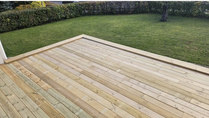 Trädäck med nygjuten ram av tryckimpregnerat trä som täcker en balkong mot en gräsmatta; plåtar och höjdjustering.