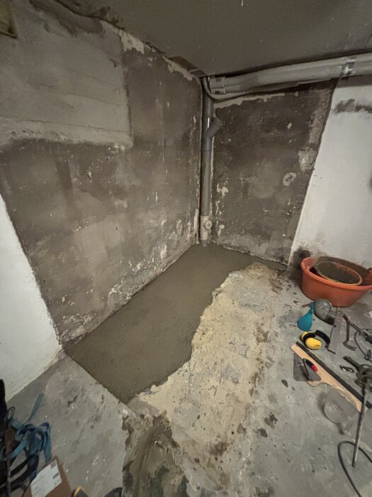 Nygjuten betongyta på golvet i ett rum med synliga avloppsrör och olika verktyg runt omkring.