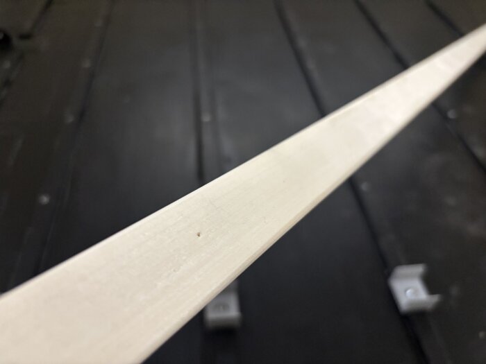 Närbild på en ljus trälist som används i golvkonstruktionen av en husvagn, med en svart bakgrund.