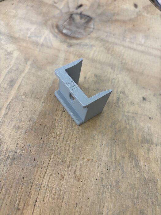 3D-printad styrningsdetalj i grått för skruvcentrering på träfiberskiva, märkt "28" för dimension.