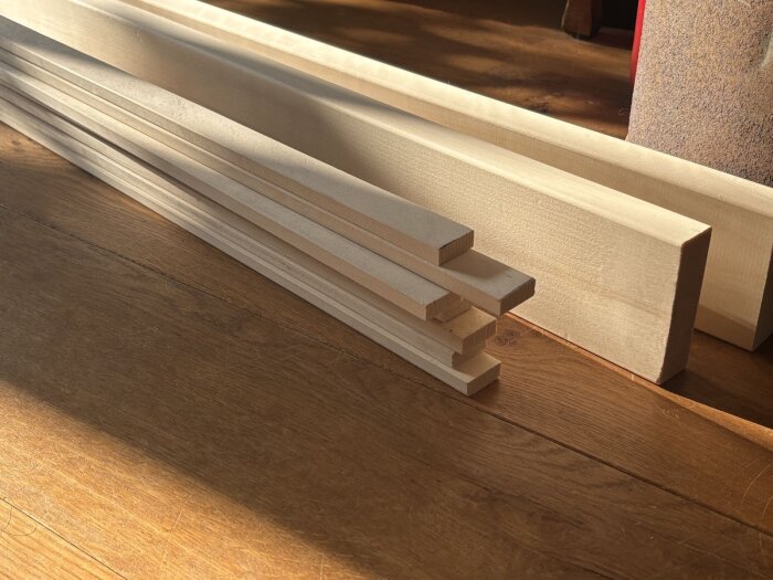 Högar av färdigkapade asp-träbitar för golvrenovering i en husvagn, liggande på ett mörkt trägolv.