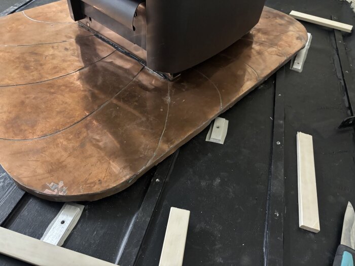 Bruna kopparplåtar monterade på svarta golvribbor i en husvagnsrenovering. Ljusa trärester spridda omkring, del av ribbmönster synligt.