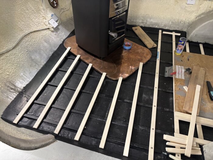 Golvläggning i husvagn med tvärgående träreglar av asp, synliga verktyg och material, påbörjad konstruktion ovanpå svart underlag.