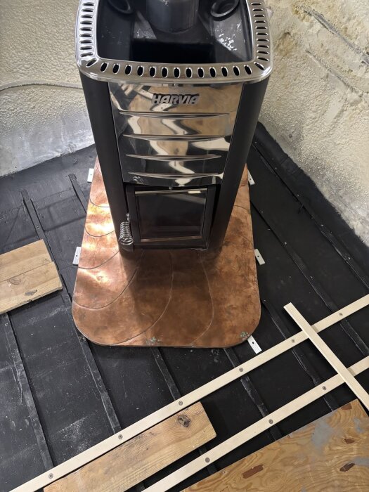 Vedspis på kopparplatta med omgivande träkonstruktion i ett husvagnsgolv under renovering.