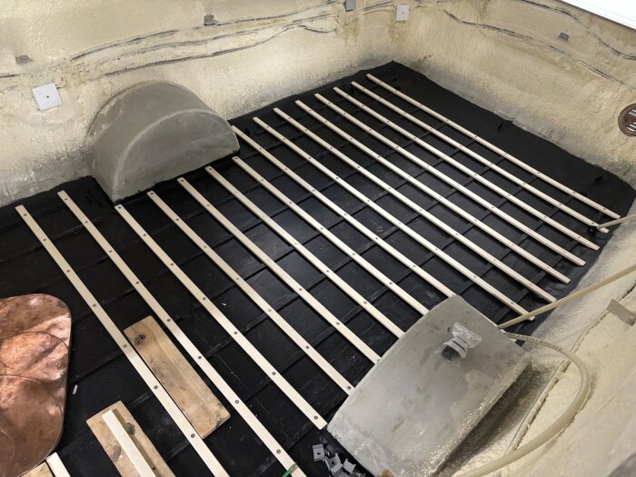 Golvet i en husvagn med tvärgående asp-ribbor monterade över ett svart undergolv, med synliga stöd och fästen.