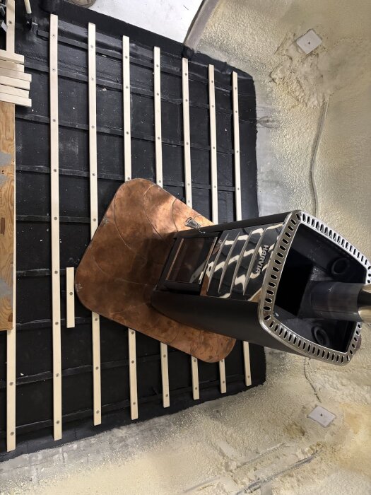 Golvet i husvagnen med fastskruvade asp-ribbor, aluminiumramar och ett bastuaggregat i mitten, synliga på svart underlag.