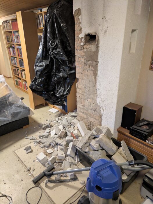 Murstock i källare med borttagen puts, murbruk och mexitegel ligger i bråte på golvet bredvid en dammsugare och svarta plastskynken.