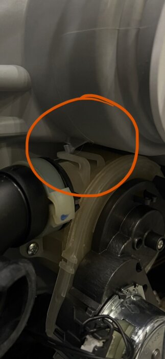 Sprucken hake på plastdel i mekanisk apparat, markerad med röd cirkel.