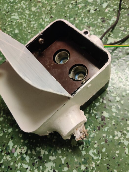 Huvudbrytare och säkringshållare för 2 huvudsäkringar i en vit låda, placerad på ett grönt golv.