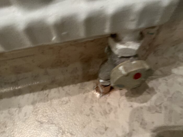 Ett elementvred från 1971 monterat på ett elementrör, med en röd markering i mitten, fotograferat i låg vinkel mot parkettgolv.