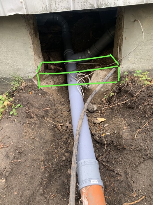 Öppning till krypgrund med rörinstallation och gröna markeringar för planerad gjutform. Originalmuren från 1936 är synlig i bakgrunden.