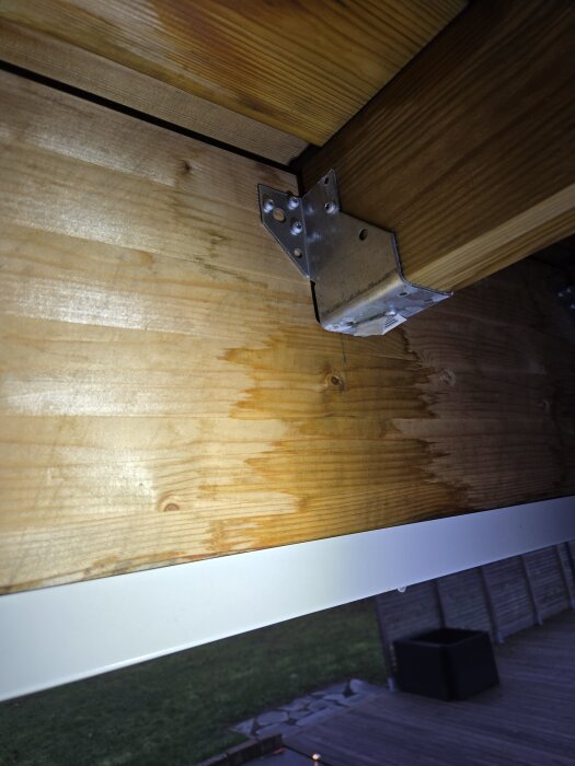 Träbjälkar med metallbeslag och en plåtlist i ett byggprojekt, träet är fuktigt och trallen är synlig i bakgrunden.