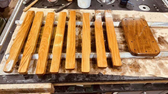 Väloljade träarmstöd till däckstolar och en förborrad ekbit ligger på en arbetsbänk efter behandling med Benar-olja. Verktyg syns i bakgrunden.