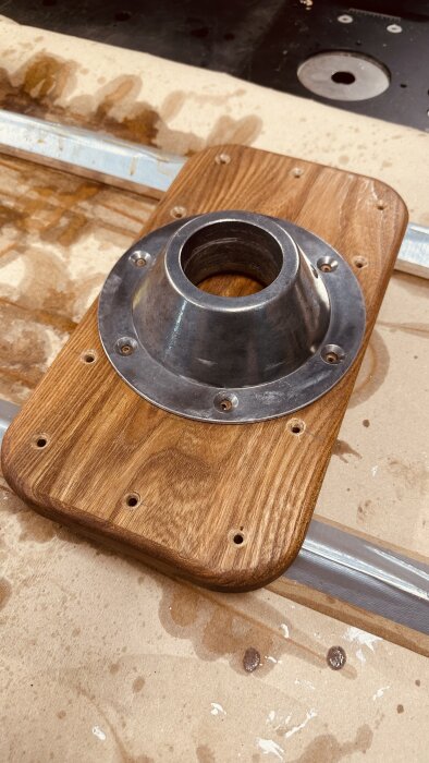 Polerat och slipat bordsfäste av metall monterat på en ny ekbit, förberedd med förborrade hål, placerad på en arbetsbänk.