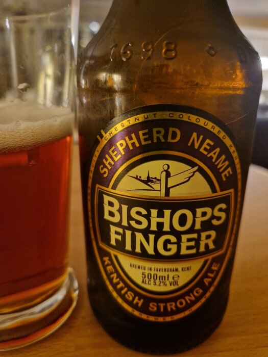 Flaska med Shepherd Neame Bishops Finger öl och ett glas öl på ett bord.