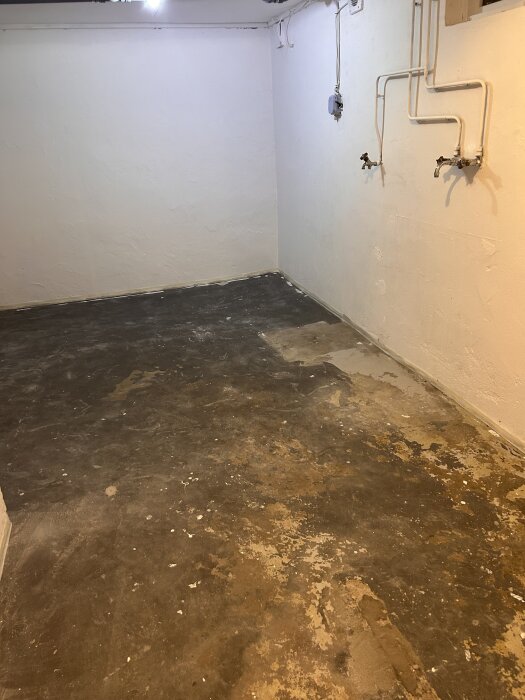Tom tvättstuga med kala väggar och betonggolv, redo för renovering och installation av bänkskiva samt tvättmaskin och torktumlare.