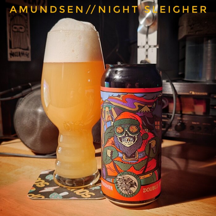 En ölburk med färgglad design och ett glas med skummande öl på ett bord; märket Amundsen, Night Sleigher Double IPA.