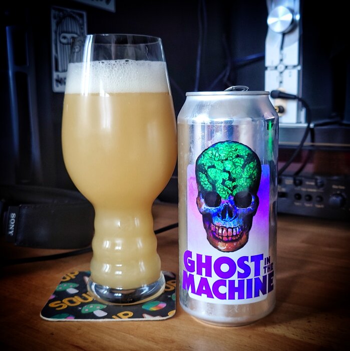 Ett glas med ljus öl bredvid en ölburk med motiv av en färgglad döskalle och texten "Ghost in the Machine".