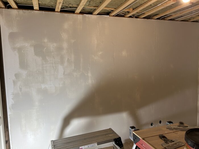 Vägg under renovering visar ojämnt applicerad spackel i ett rum med träpanel i taket och arbetsbänk framför.