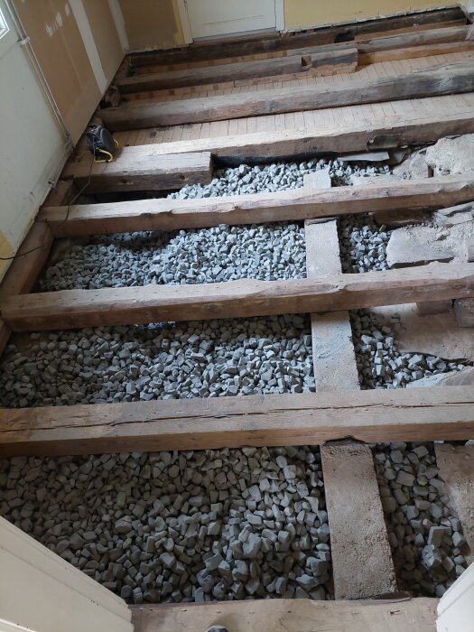 Trägolv uppbrutet med synliga bjälkar och stenfyllning i bjälklaget, del av diskussion om installation av golvvärme under massiv grangolv.