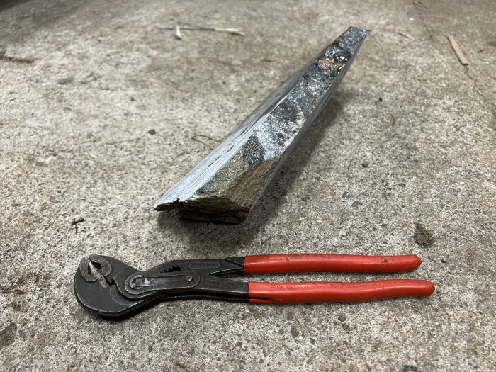 En bit röd granit ligger på marken, bredvid en polygrip med röda handtag, vilket visar storleken på granitstycket.