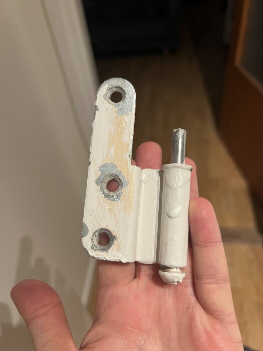 Gammalt vitt dörrgångjärn från Assa Abloy hålls i en hand, med tre hål för skruvar.