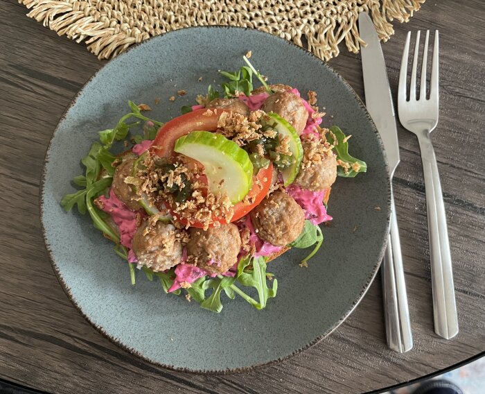 Köttbullsmacka med sallad, rödbetssallad, och stekt lök på en tallrik. Bestick syns bredvid tallriken.