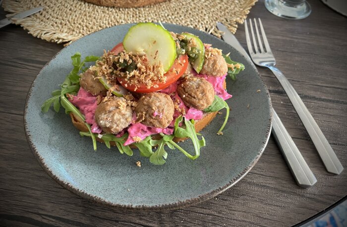 Köttbullsmacka på tallrik med sallad, rödbetssallad, tomat, gurka och rostad lök.